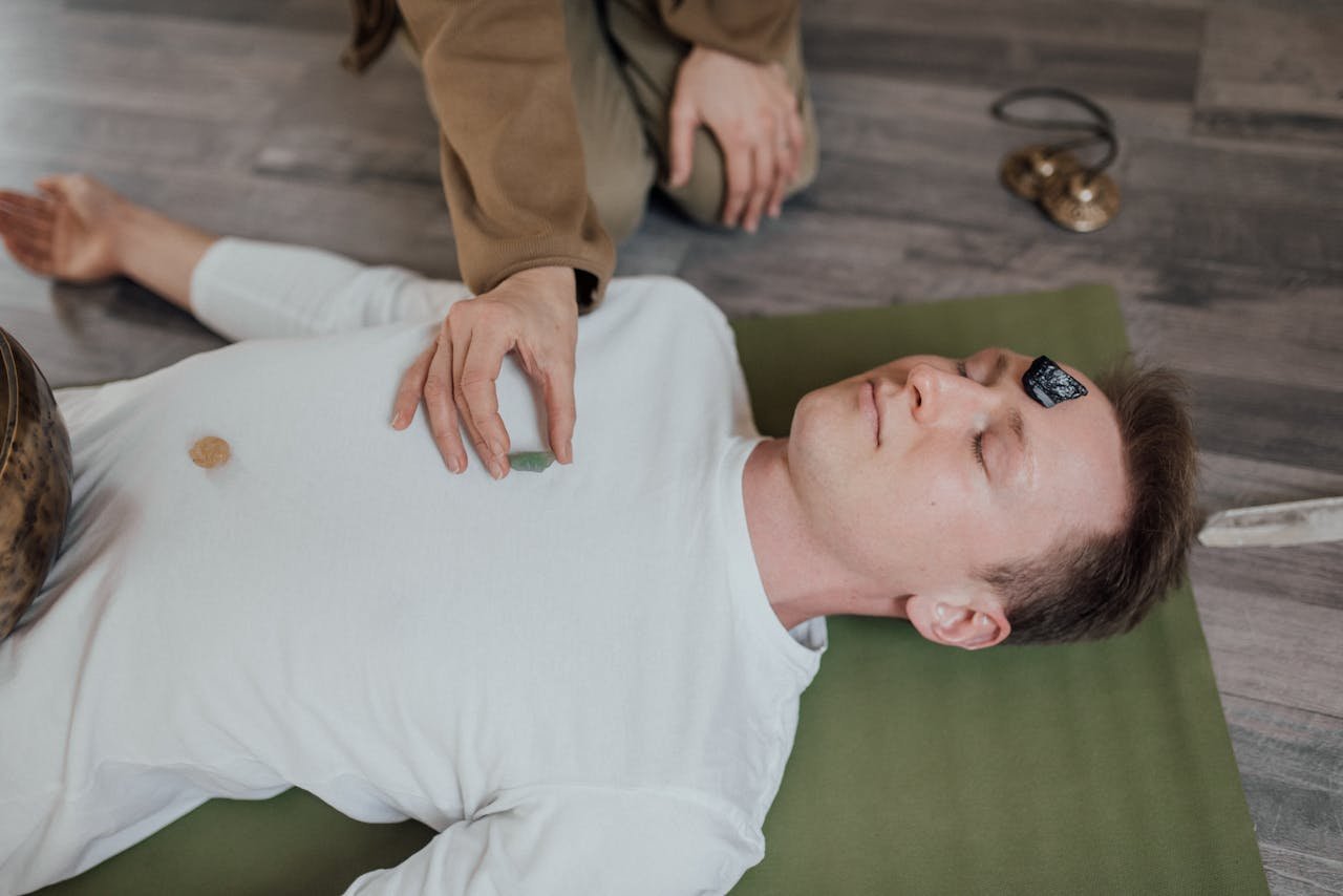 A man lies peacefully with crystals during a chakra healing meditation session indoors.